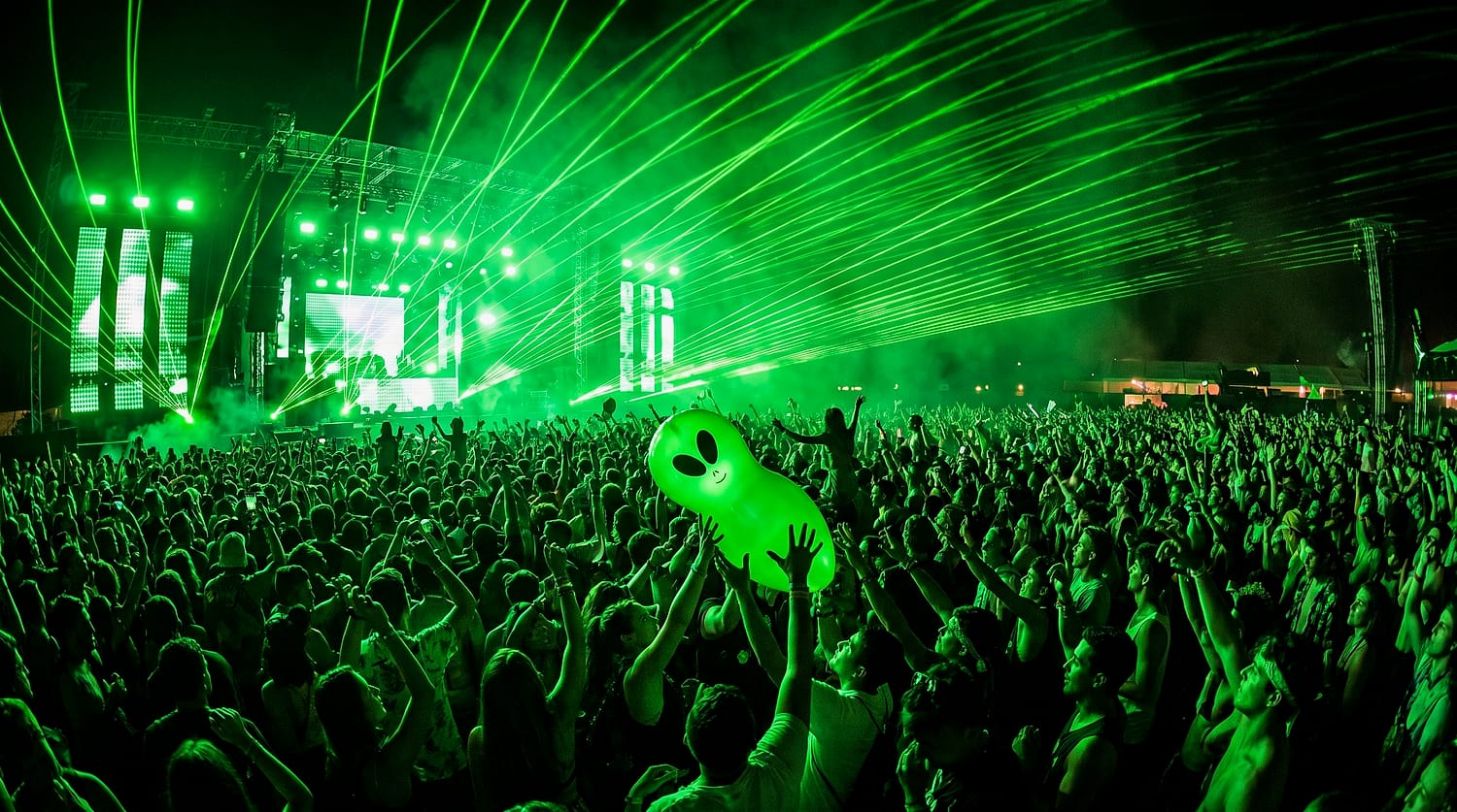 A dense festival crowd under green lasers at night